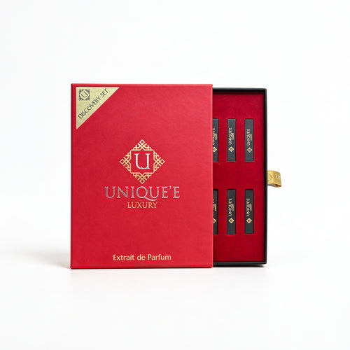 A luxury perfume discovery set in a red box, with the lid standing open next to the box interior showing several slim black perfume strips with gold lettering.