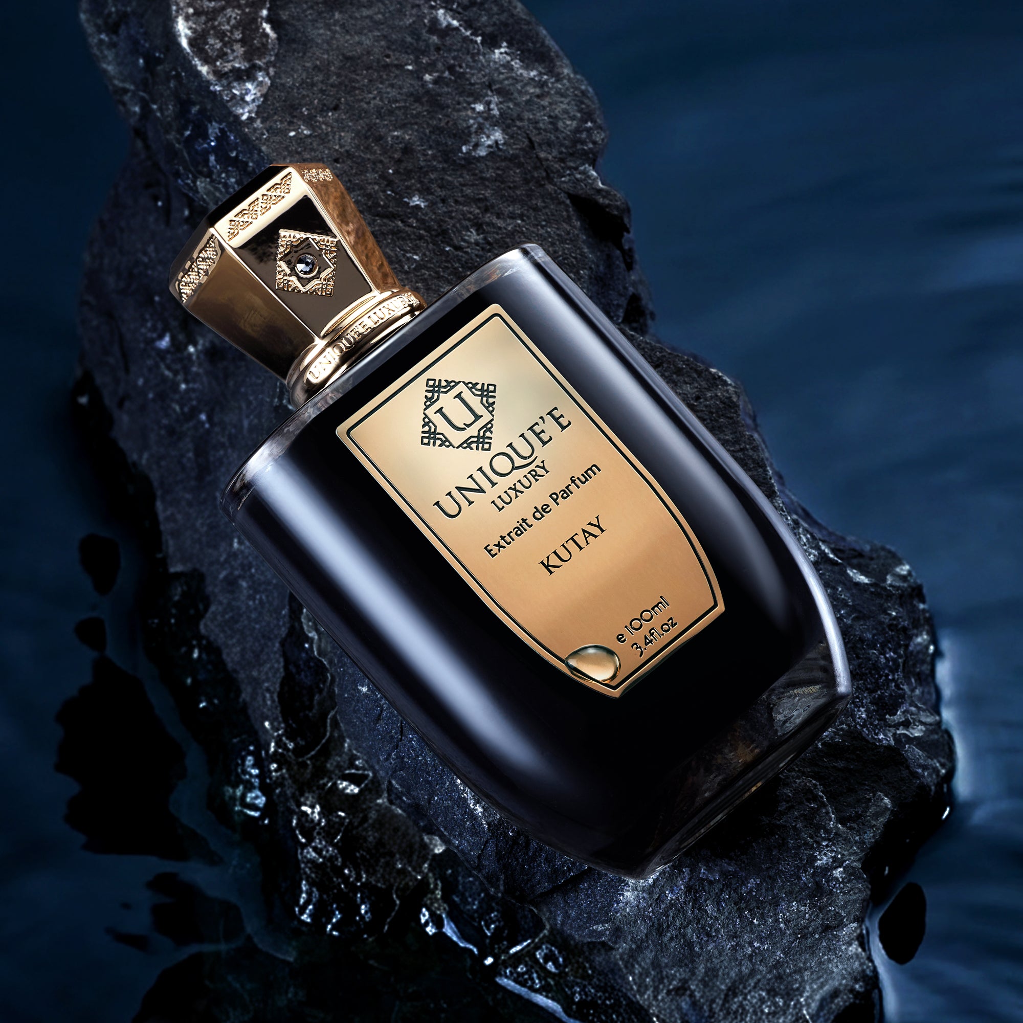 A black bottle of 'KUTAY 100 ml' perfume with a gold label and cap, under the brand name 'UNIQUE E LUXURY'. The bottle is filled with a yellowish liquid and has a luxurious appearance.