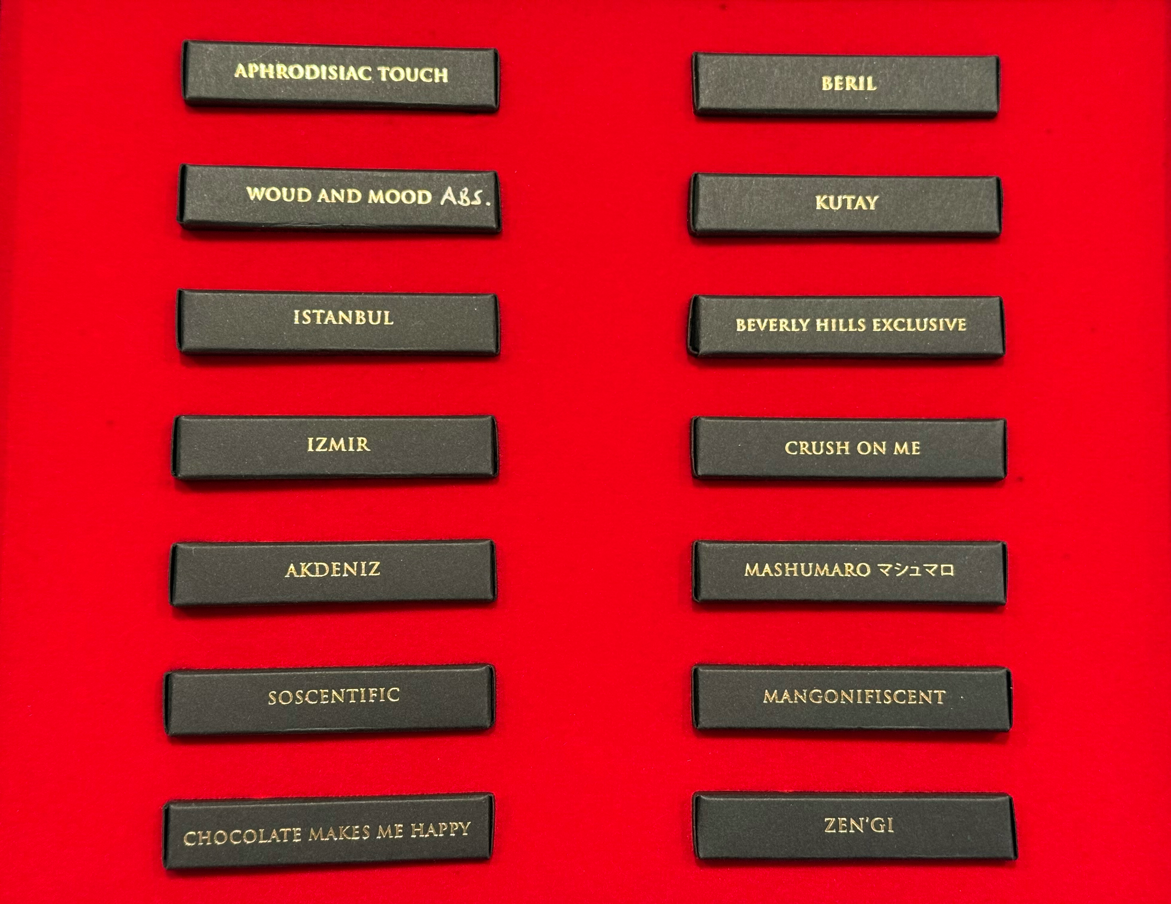 A luxury perfume discovery set in a red box, with the lid standing open next to the box interior showing several slim black perfume strips with gold lettering.